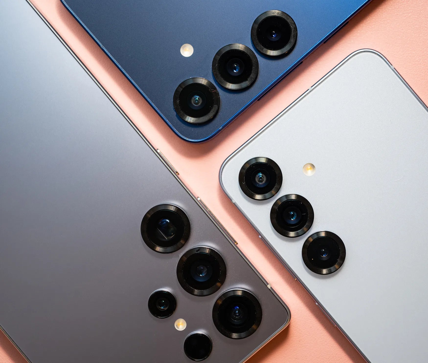 Three smartphones with camera modules on a pink and blue gradient background